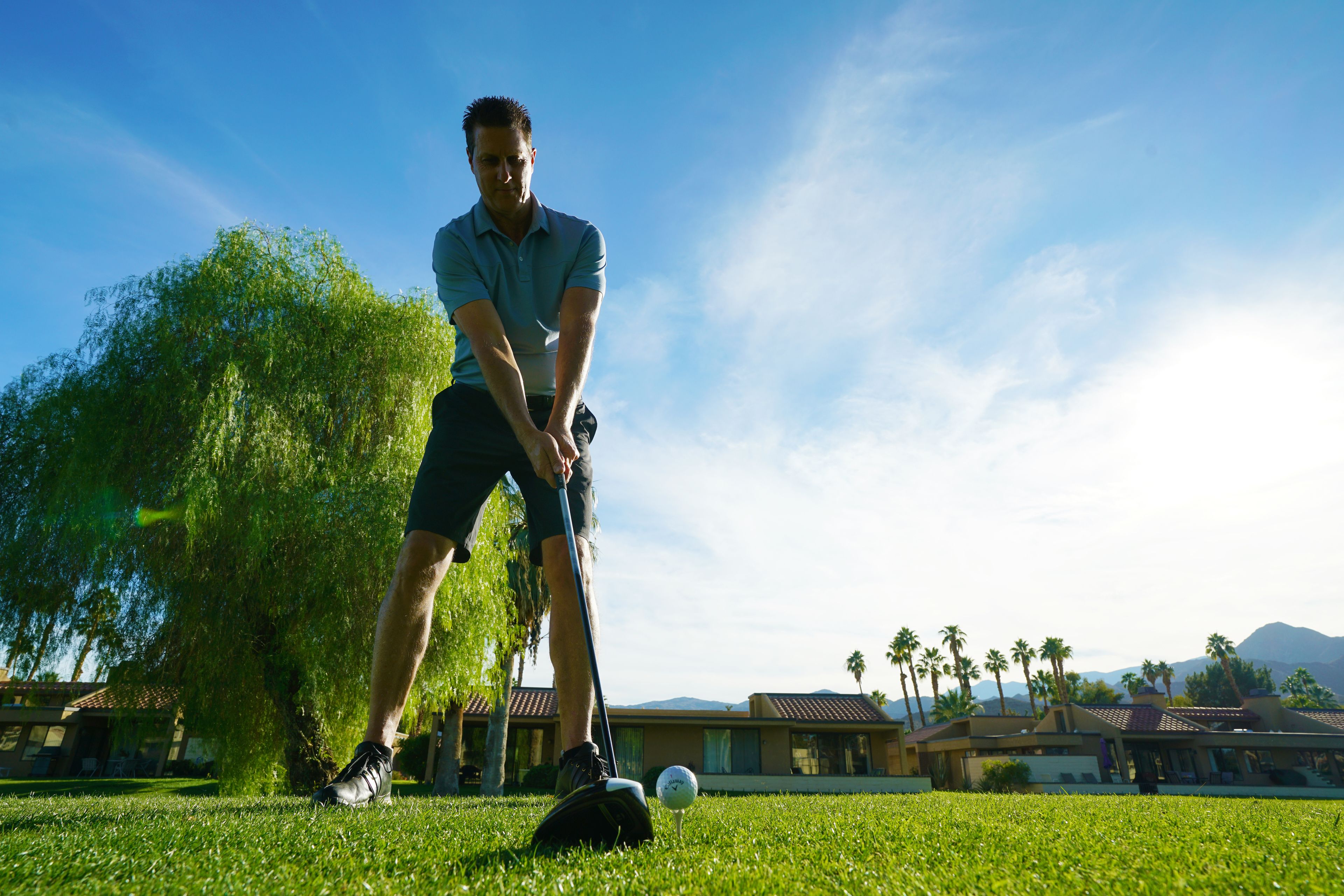 A golf course with a clear sky, palm trees, and a building in the background.