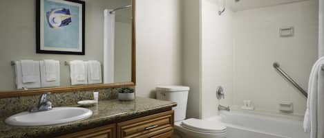 A modern bathroom with a granite countertop sink, a white toilet, a bathtub with a showerhead, and a framed artwork on the wall.