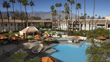 A resort with a swimming pool, lounge chairs, and palm trees.