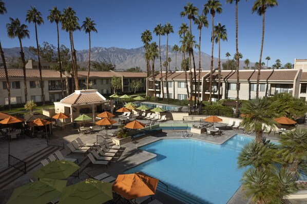 A resort with a swimming pool, lounge chairs, and palm trees.