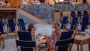 Un restaurant situé en bord de mer, avec une terrasse, un mur en pierre et une vue sur l’océan.