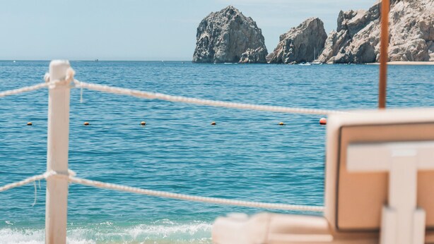 Une plage avec un parasol blanc, une chaise longue et une barrière faite de cordes.