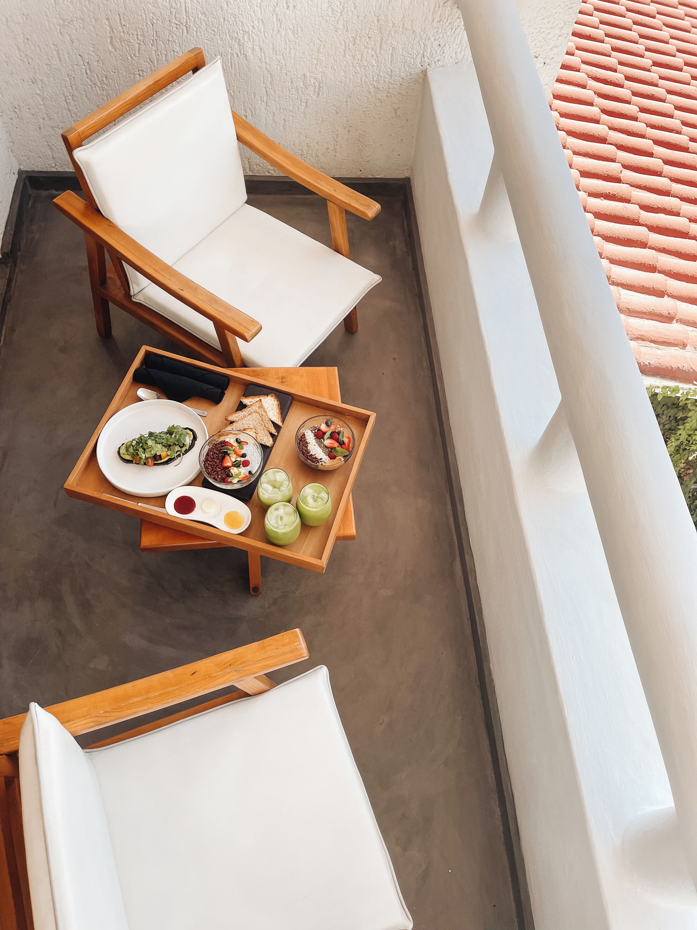 A balcony with two wooden chairs and a table set with food and drinks.