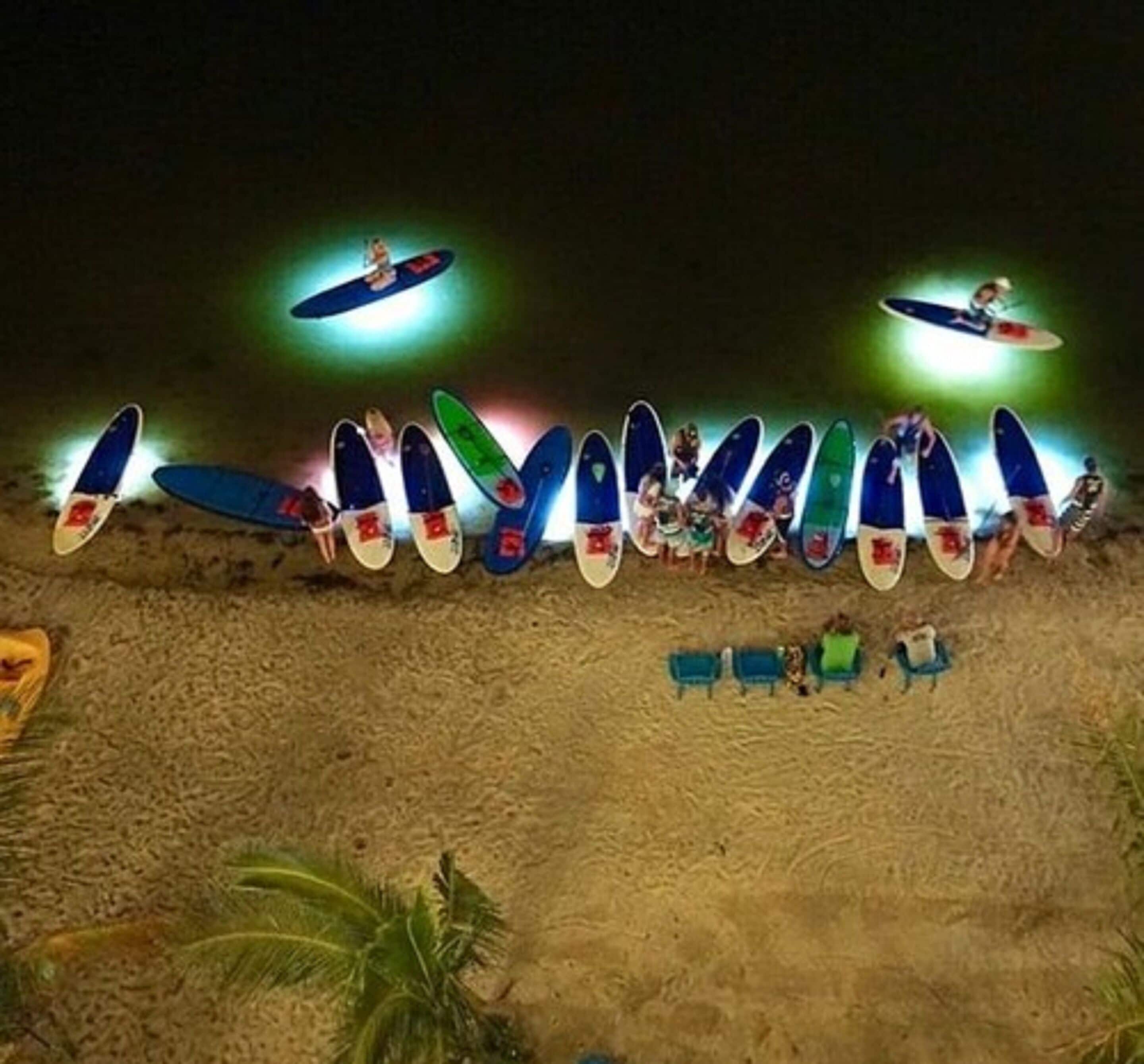 Eine Reihe von Surfbrettern liegt nachts an einem sandigen Strand aufgereiht.