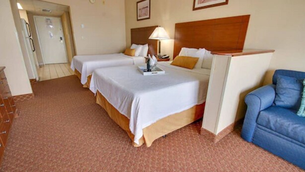 A hotel room with two single beds, a wooden headboard, a blue armchair, and a small table with a lamp.