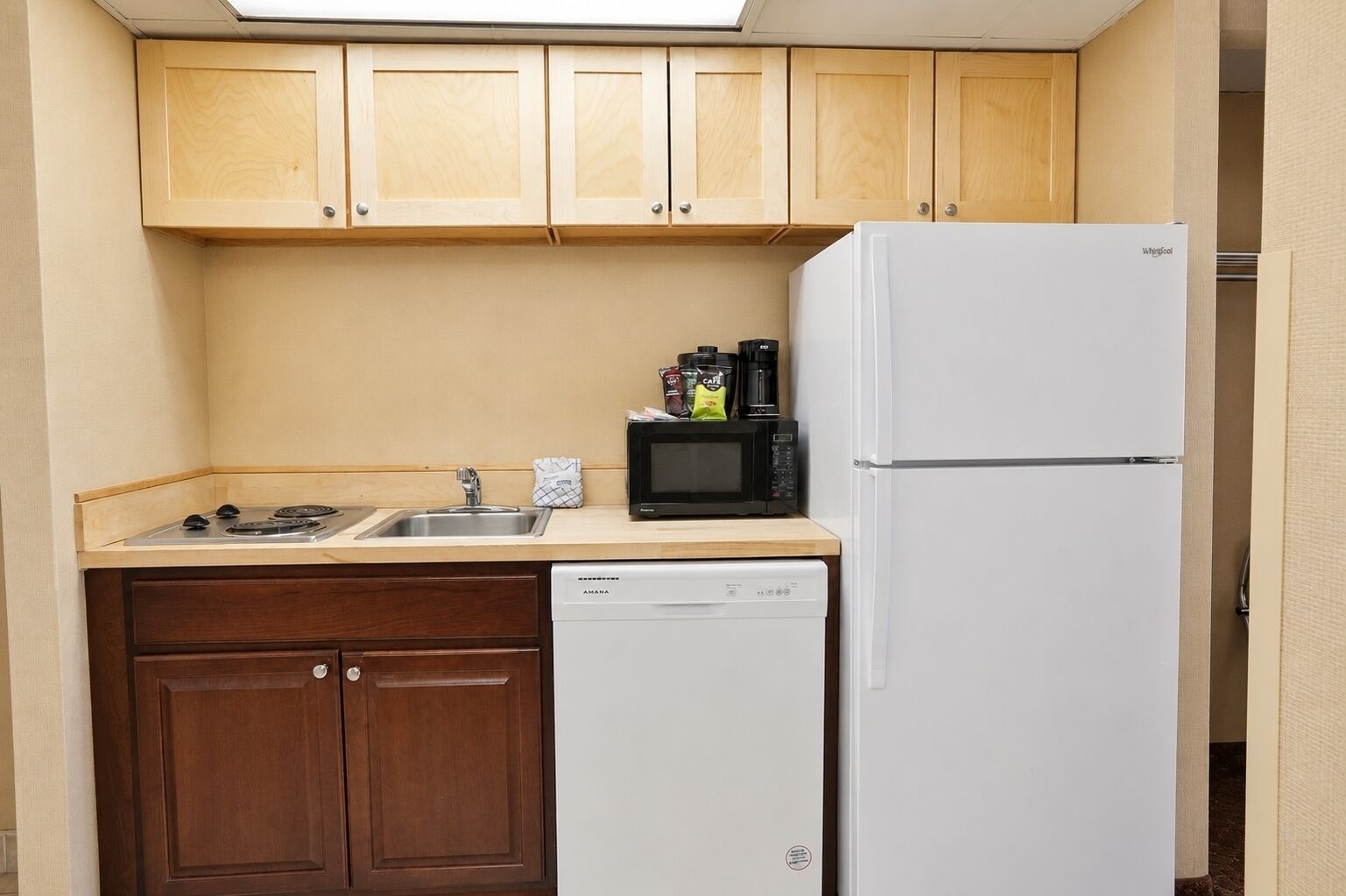 A compact kitchen with wooden cabinets, a white dishwasher, a white refrigerator, a microwave, and a gas stove.