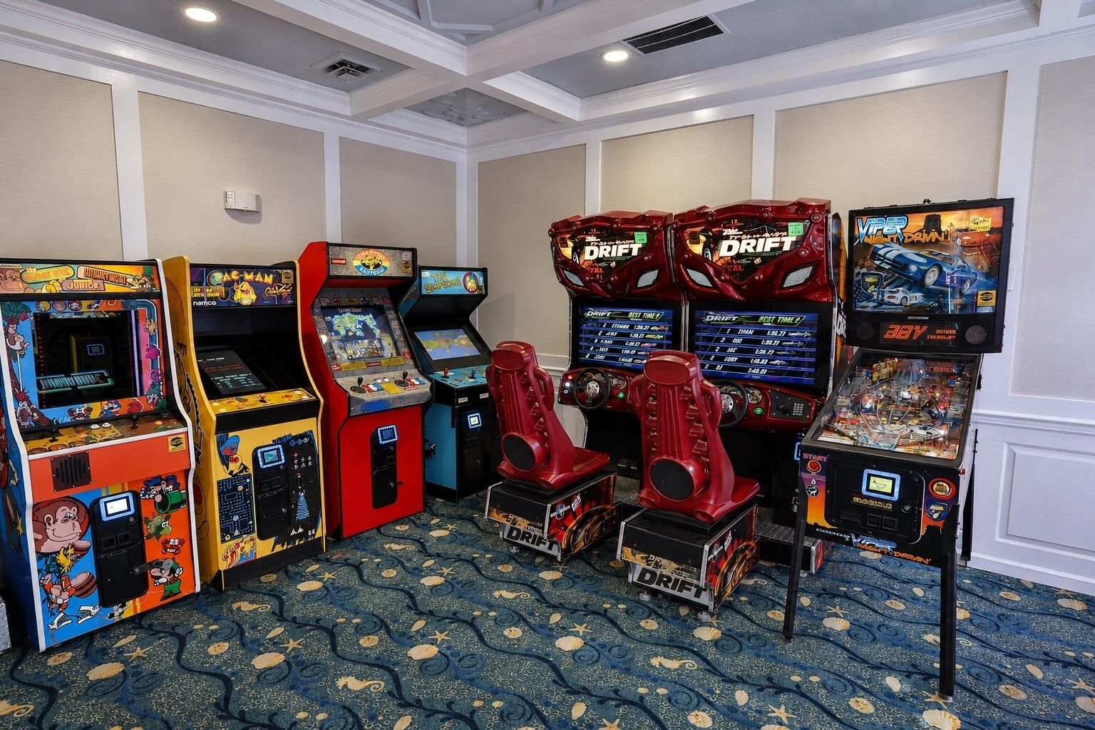 A room with arcade machines, carpeted floor, and white walls.