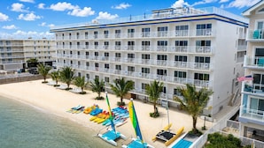 A hotel with multiple balconies, a beach with kayaks, and a flag. - Princess Bayside Beach Hotel (Ocean City)