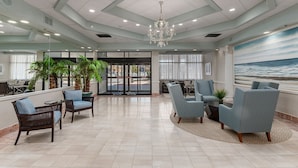 A spacious lobby with a high ceiling, a chandelier, and seating areas with blue upholstered chairs. - Princess Bayside Beach Hotel (Ocean City)