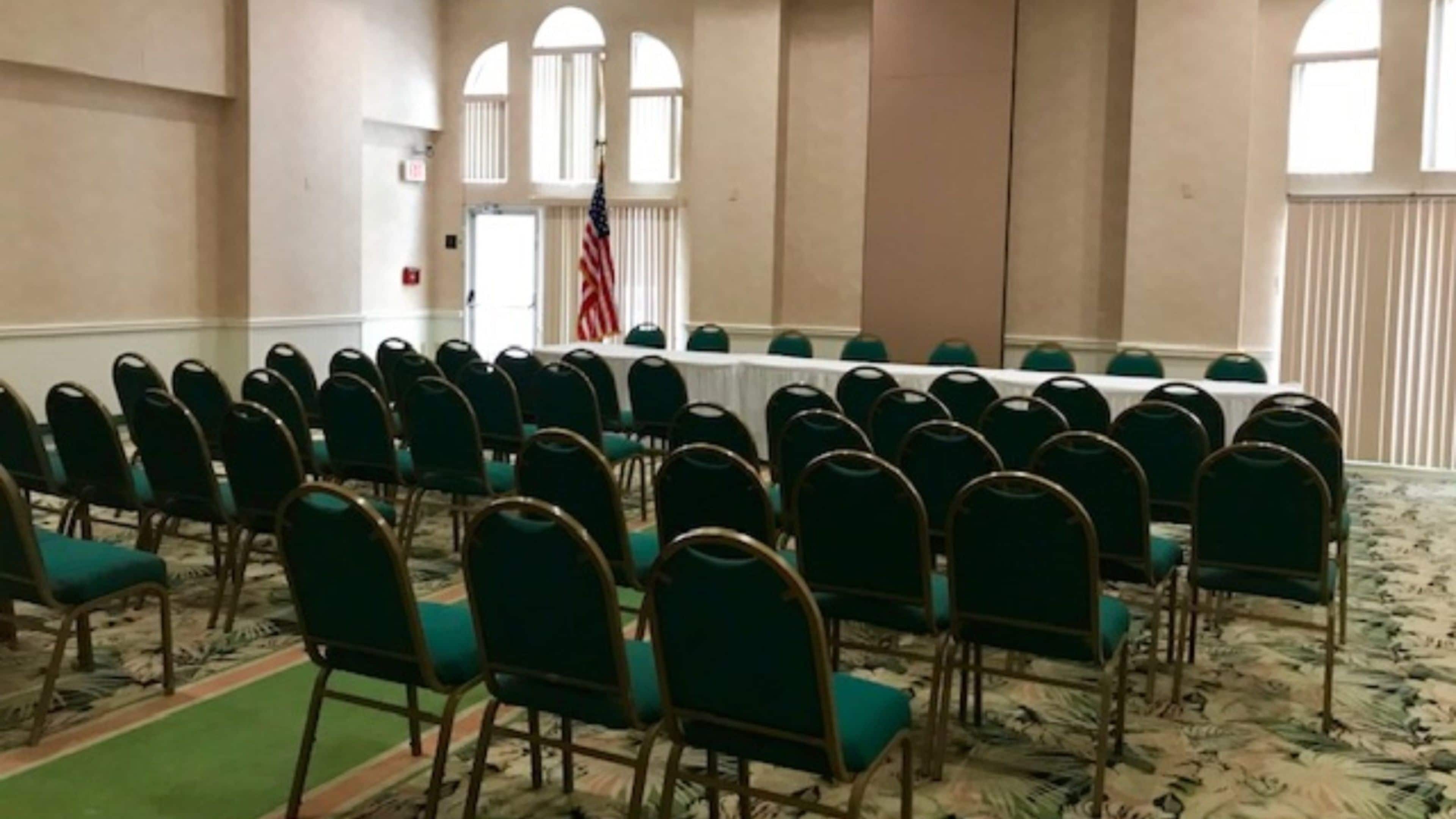 A conference room with rows of green chairs, a long table, and an American flag.