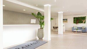 A modern reception area with a doormat, a potted plant, a wall-mounted light, and a seating area with a blue sofa. - Club La Costa at the Paradise Club (Adeje)