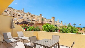 A terrace with outdoor seating, a table, and a view of a hillside residential area. - Club La Costa at the Paradise Club (Adeje)