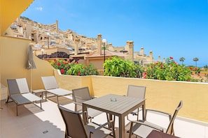 A terrace with outdoor seating, a table, and a view of a hillside residential area. - Club La Costa at the Paradise Club (Adeje)