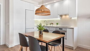 A modern kitchen with white cabinets, a wooden dining table, black chairs, and a hanging pendant light. - Club La Costa at the Paradise Club (Adeje)