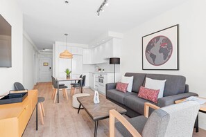 En moderne stue med en grå sofa, et træbord og et spiseområde med et hvidt bord og stole.