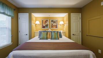 A hotel room with a large bed, two wall-mounted lamps, and two framed floral paintings above the bed.