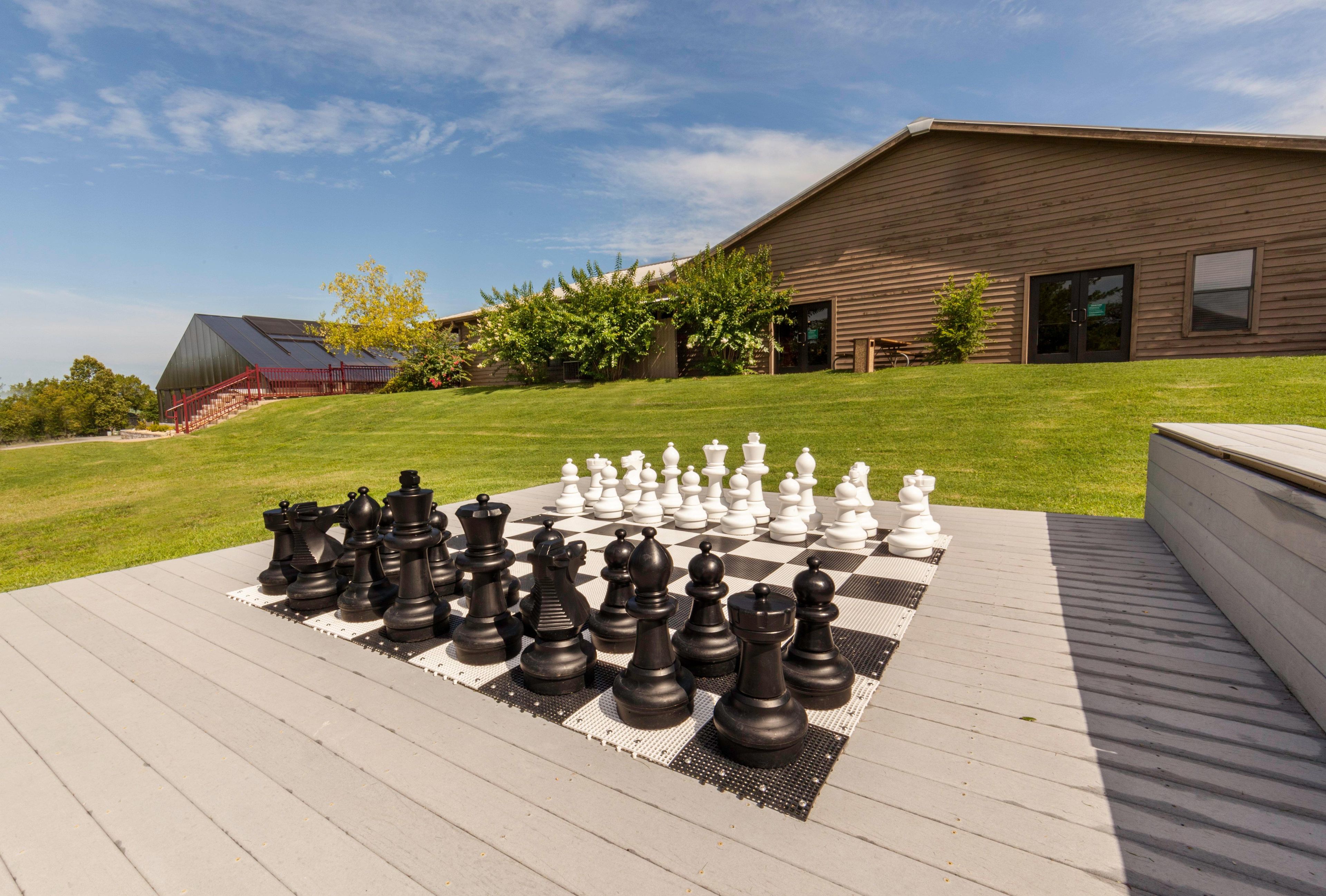 A chessboard set up on a wooden deck with a house in the background.