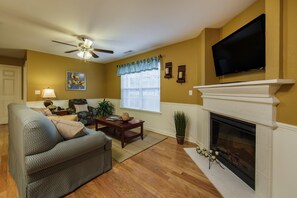 A living room with a fireplace, a ceiling fan, a television, and a window with blinds. - Holiday Hills Resort at Branson (Branson)