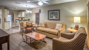 A living room with a sofa, armchair, wooden coffee table, dining table with chairs, kitchen area with appliances, and a ceiling fan. - Holiday Hills Resort at Branson (Branson)