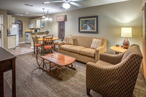 A living room with a sofa, armchair, wooden coffee table, dining table with chairs, kitchen area with appliances, and a ceiling fan. - Holiday Hills Resort at Branson (Branson)