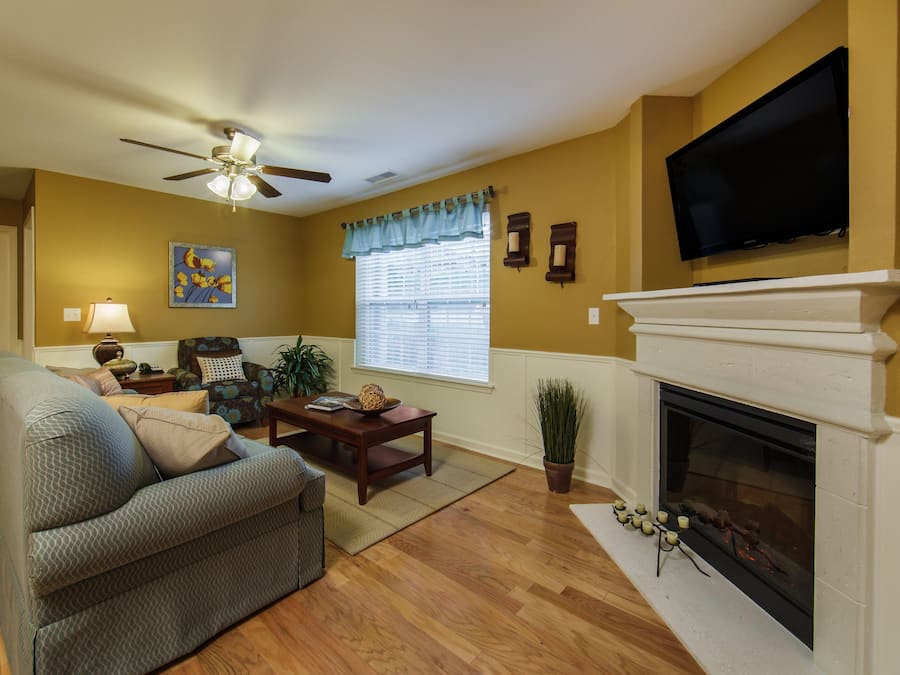 A living room with a sofa, a coffee table, a fireplace, a television, and a ceiling fan.