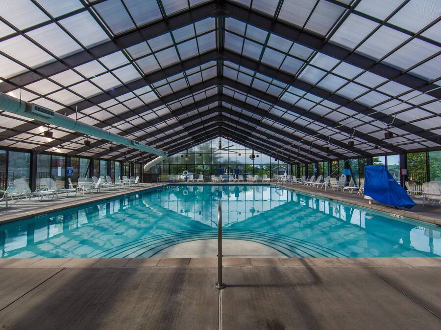 A covered swimming pool with clear blue water, surrounded by lounge chairs and a blue slide.