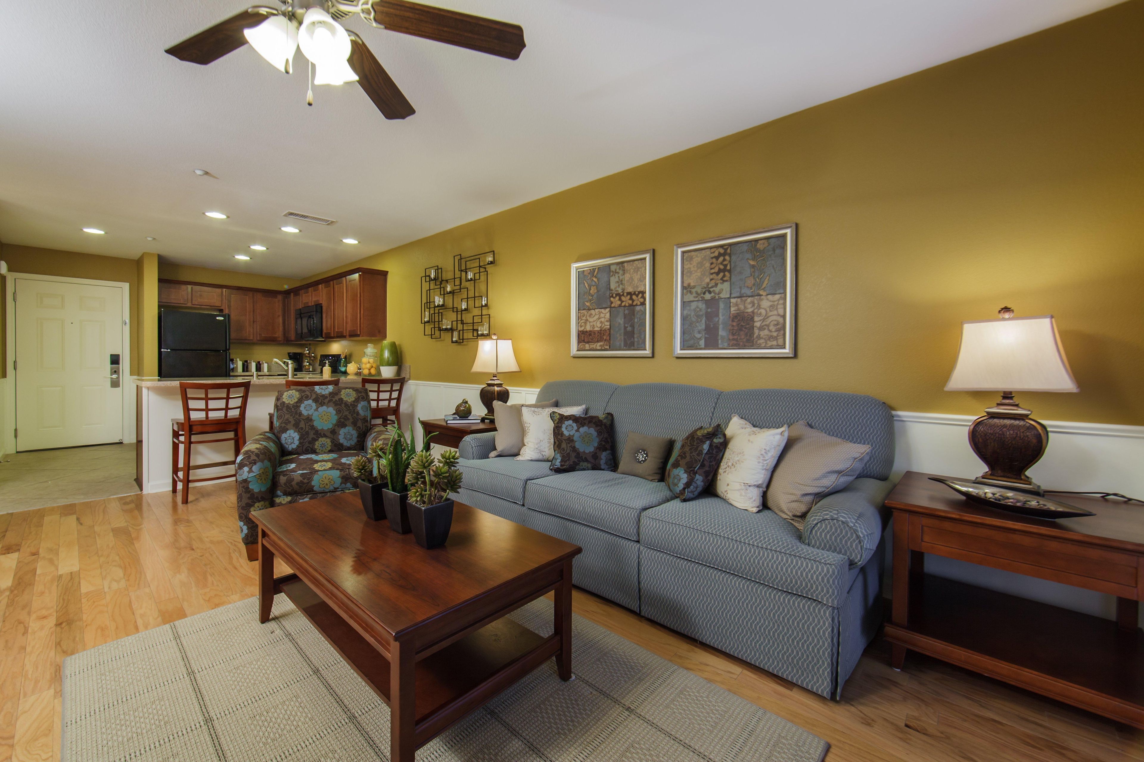 A living room with a sofa, coffee table, and a dining area with chairs and a kitchen in the background.