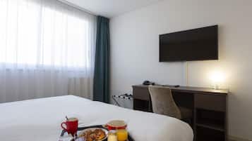 Een hotelkamer met een bed, een bureau, een televisie en een ontbijtplateau met croissants, sap en koffie.