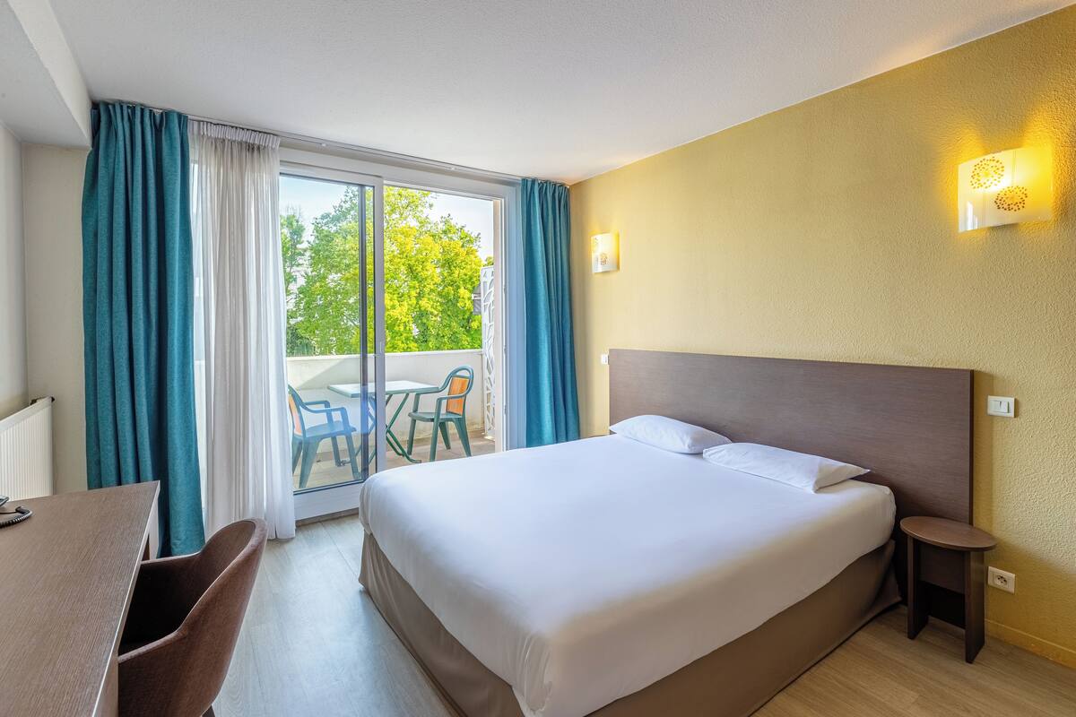 Ein Hotelzimmer mit einem großen Bett, einem Schreibtisch und Blick ins Freie durch eine Schiebetür.