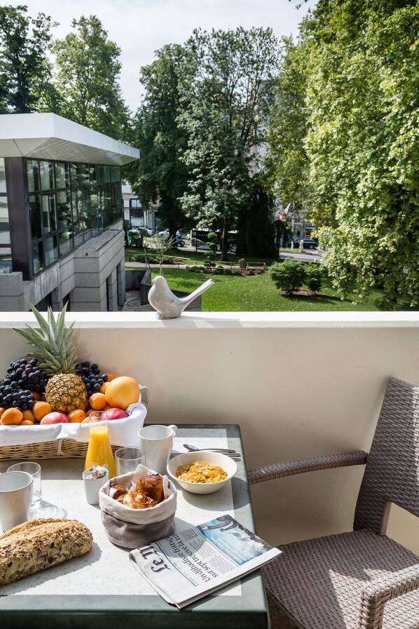 Un balcon avec des éléments pour le petit-déjeuner, un journal et une vue sur un immeuble et des arbres.