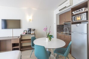 Une cuisine compacte équipée d’un four à micro-ondes, d’un réfrigérateur et d’un évier. On y trouve une table à manger avec des chaises et une orchidée en pot. Un téléviseur à écran plat est fixé au mur.