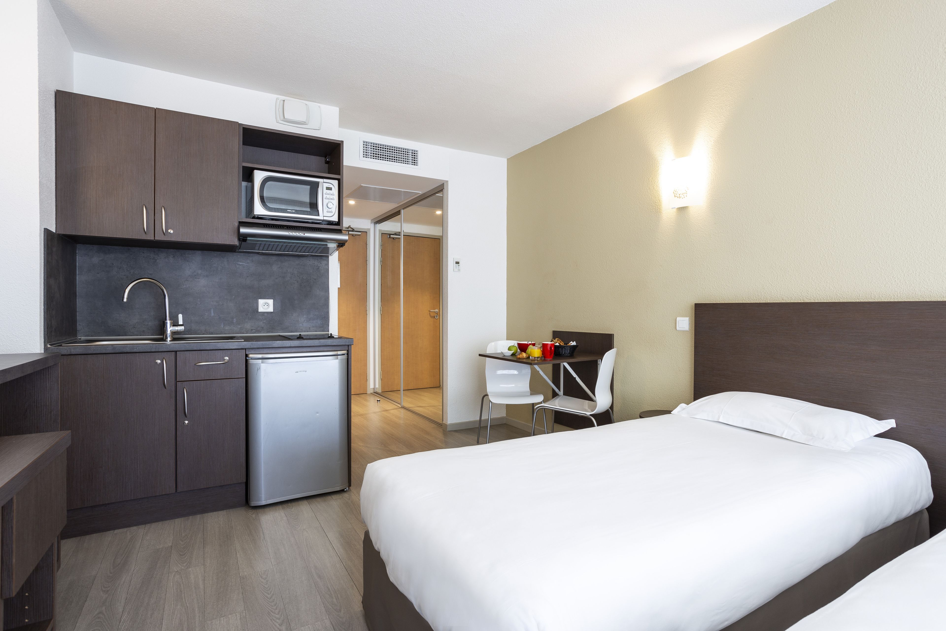 A compact hotel room with a kitchenette, a bed, and a small desk with a chair.