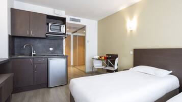 A compact hotel room with a kitchenette, a bed, and a small desk with a chair.