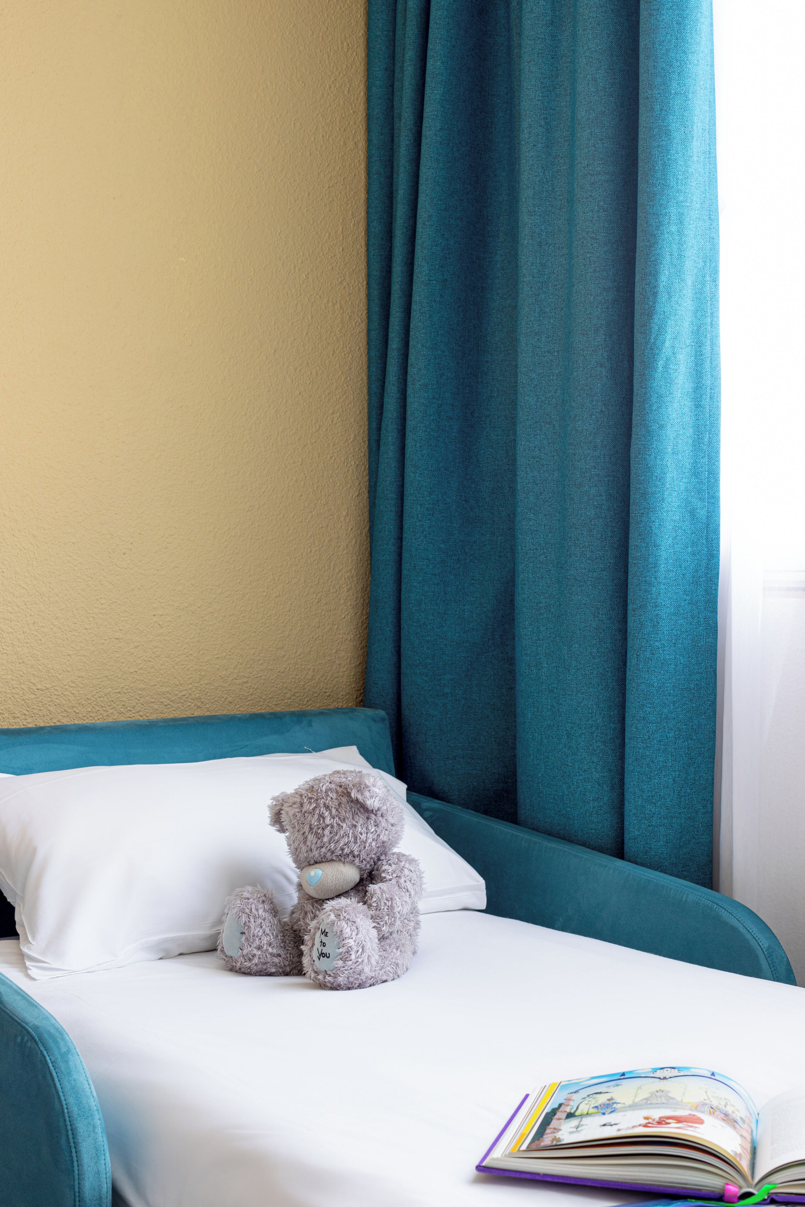 A bed with a teal headboard, a white pillow, and a plush teddy bear.