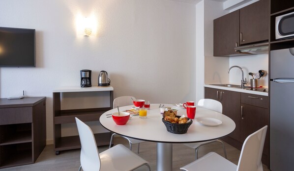 Cocina moderna con comedor, equipada con cafetera, hervidor y provisiones para el desayuno sobre la mesa.