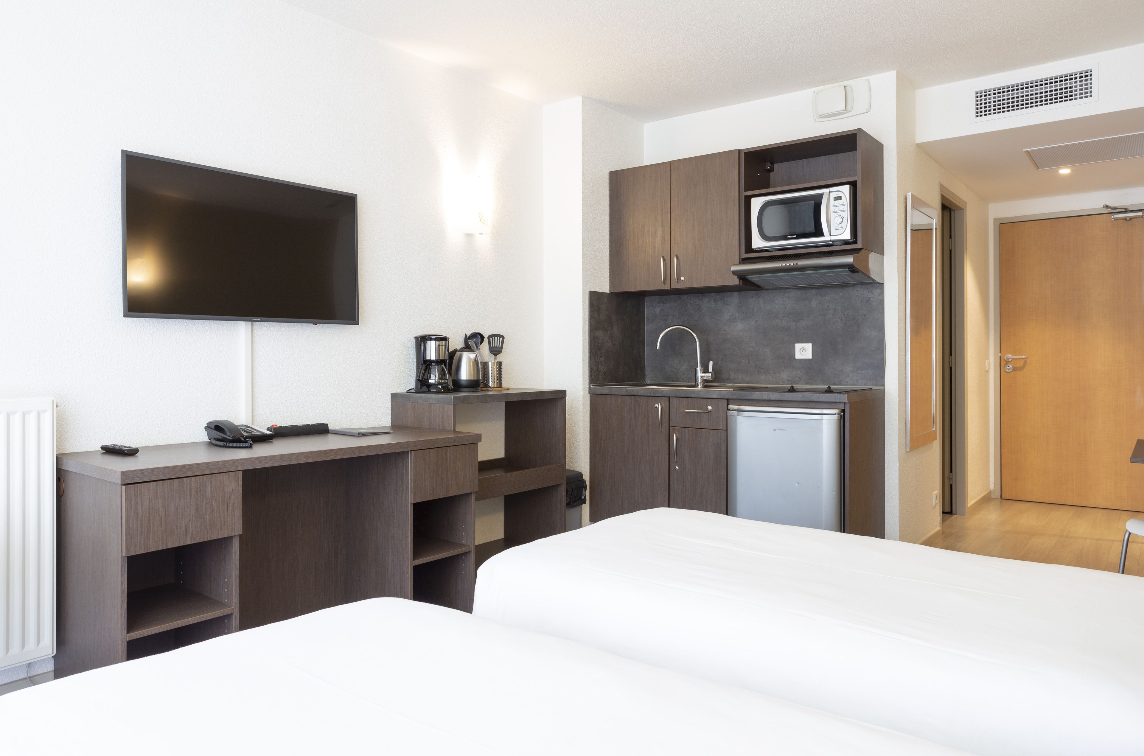 Une chambre d’hôtel comprenant un lit, un bureau avec un téléviseur à écran plat, une kitchenette équipée d’un four à micro-ondes et un petit réfrigérateur.