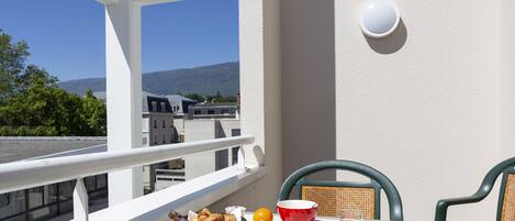 Un balcón con comida para el desayuno, vistas a edificios y montañas, y una barandilla blanca.