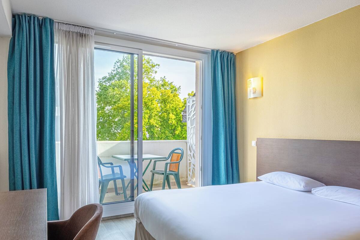 Ein Hotelzimmer mit Bett, Schreibtisch und Stuhl. Es gibt einen Balkon mit Tisch und Stühlen.