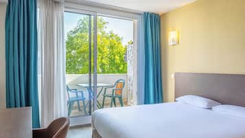 A hotel room with a bed, a desk, and a chair. There is a balcony with a table and chairs.