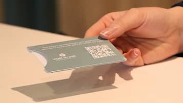 A hand holding a card with a QR code and text, placed on a table.