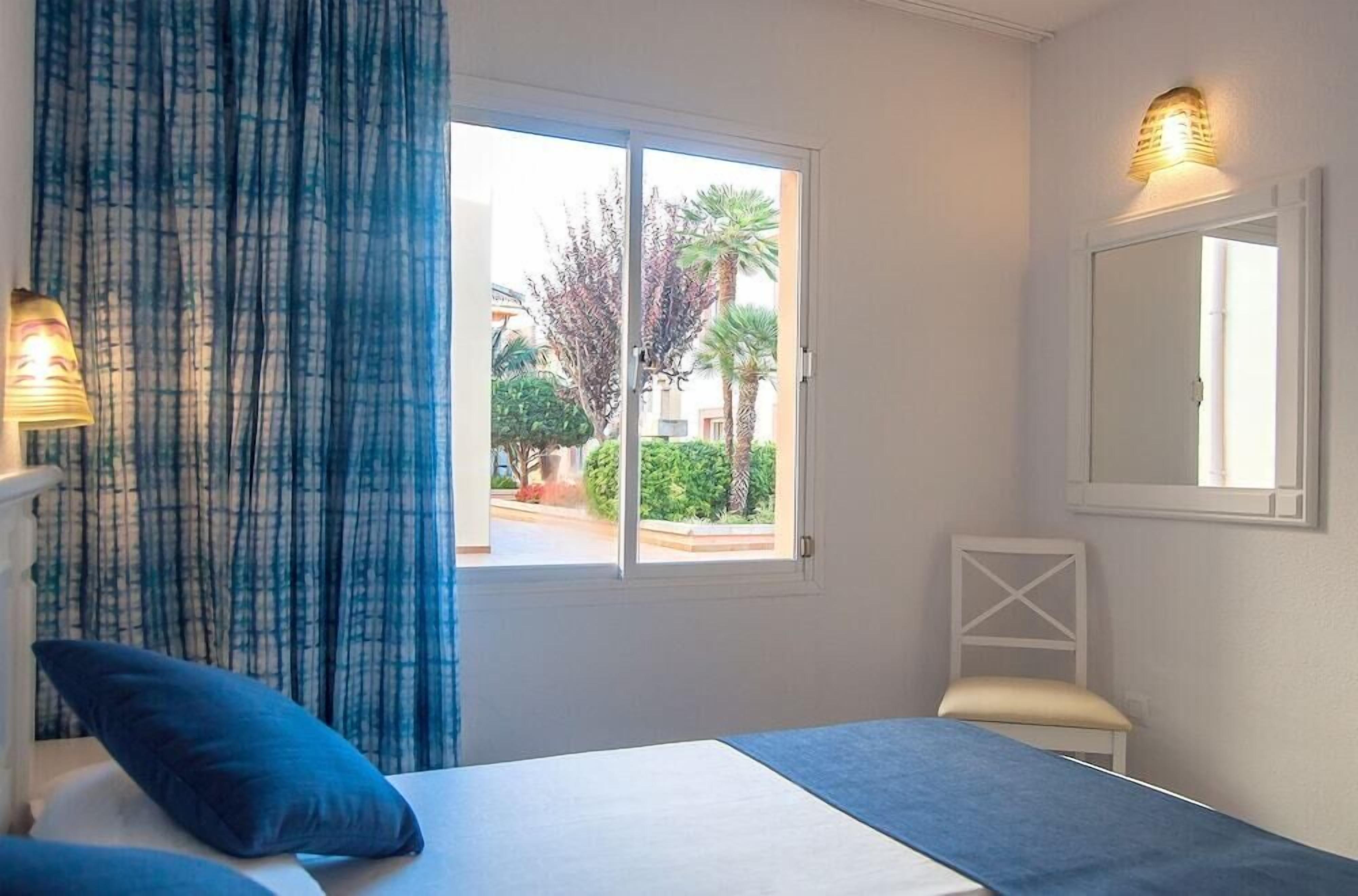 Een slaapkamer met een bed, een raam met gordijnen, een stoel en een wandlamp.