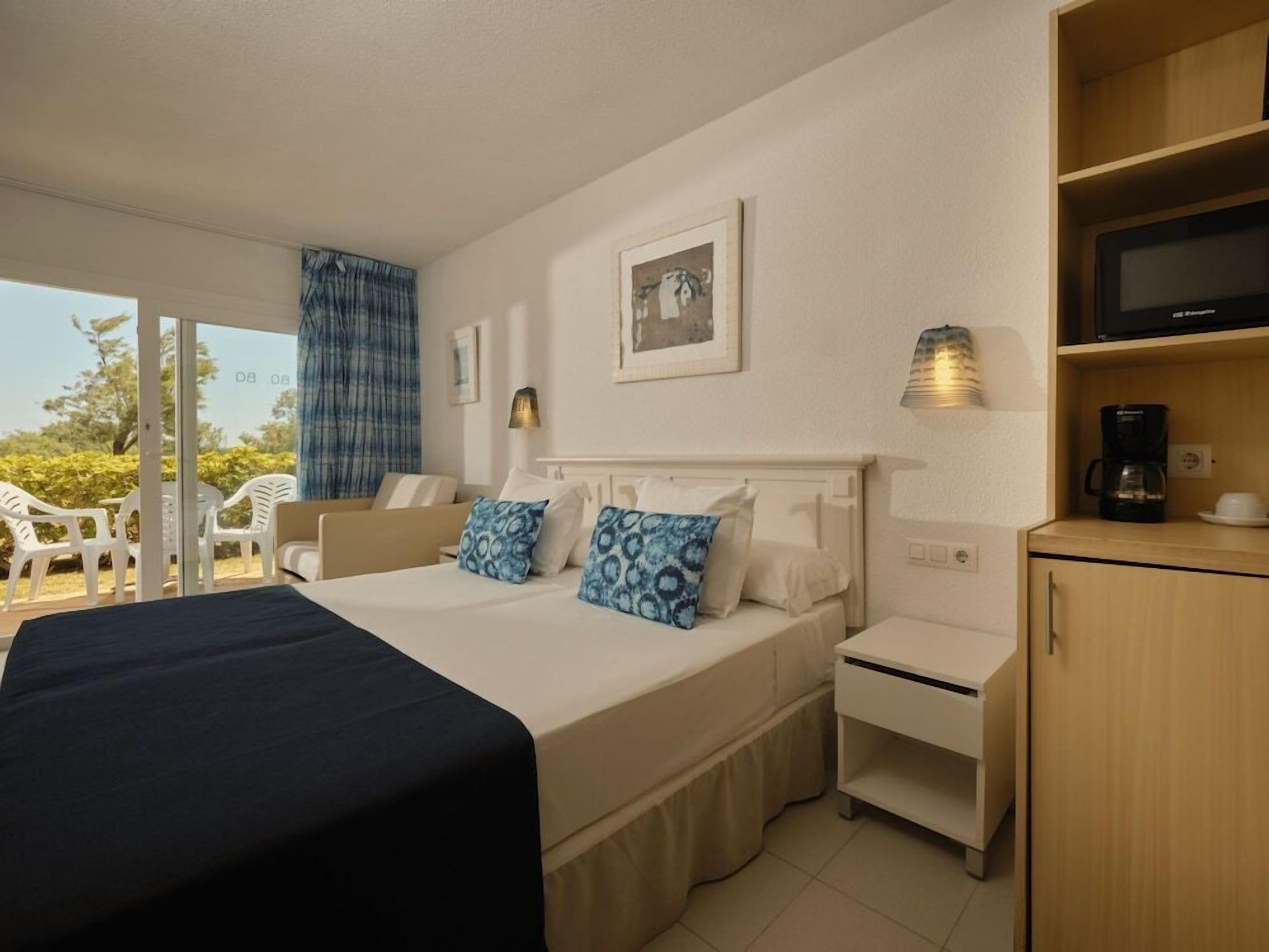 A hotel room with a bed, a bedside table, a lamp, a television, and a coffee maker.
