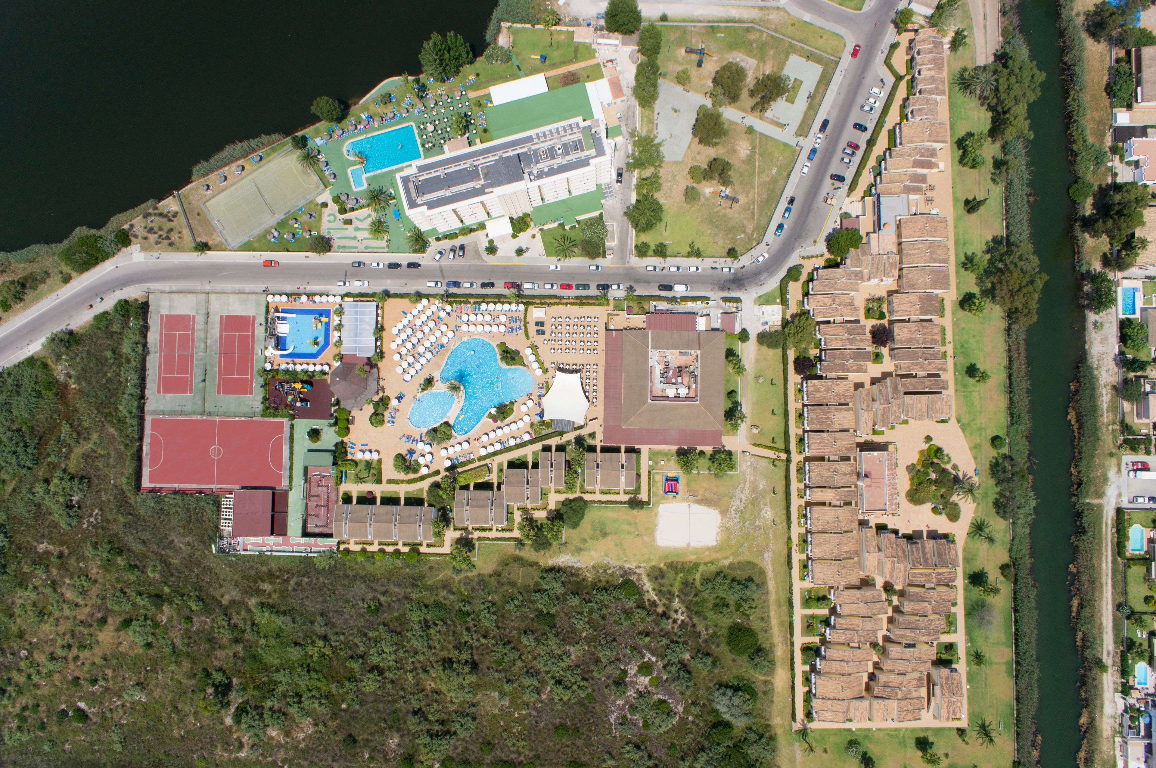 Vista aèria d'un complex turístic amb piscina, pistes de tennis i zona d'aparcament.