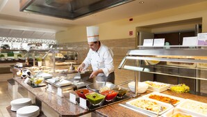 Montaje de bufé con diferentes alimentos y un chef preparándolos.