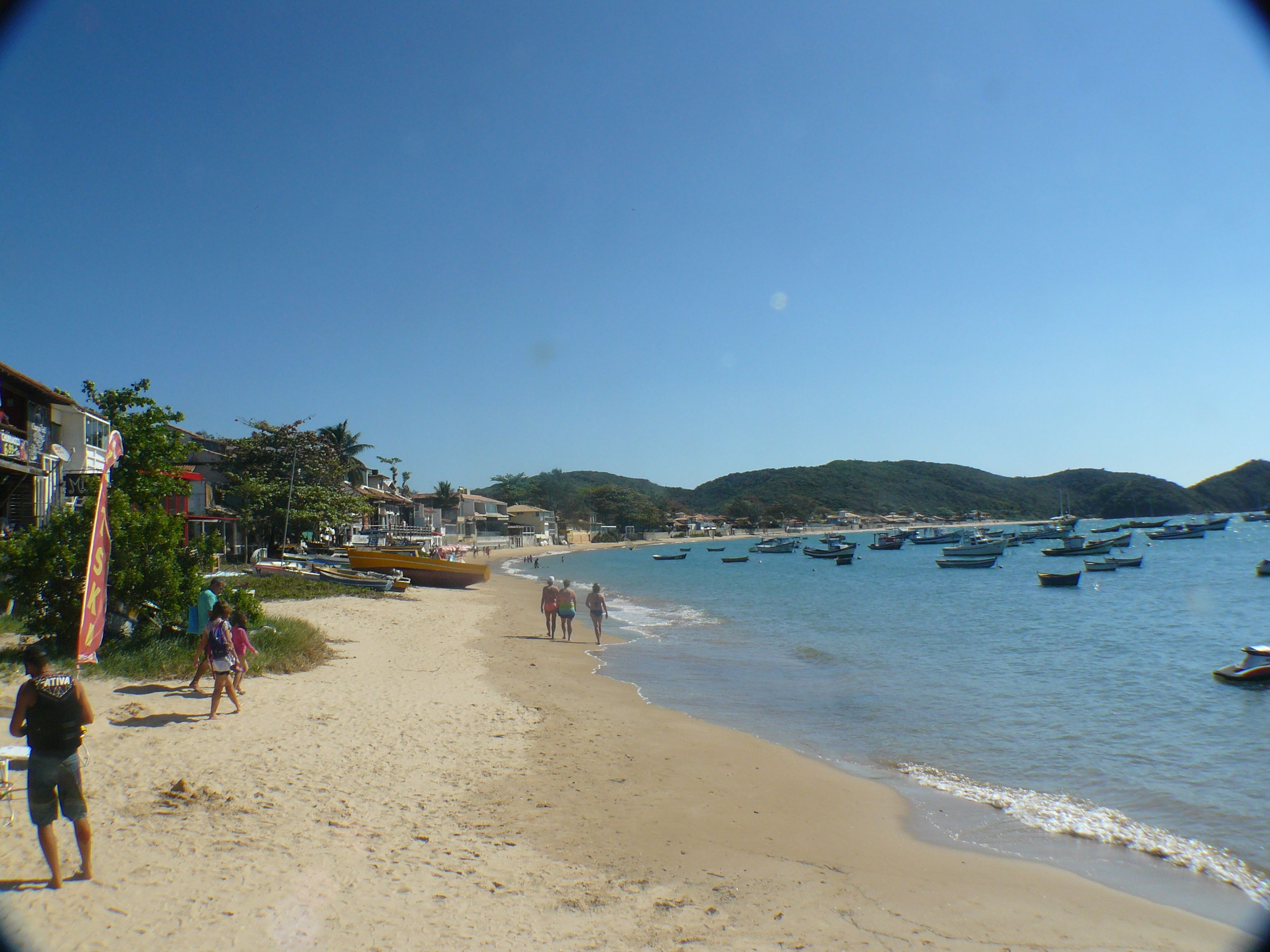 A beach with boats, people walking, and buildings along the shore.