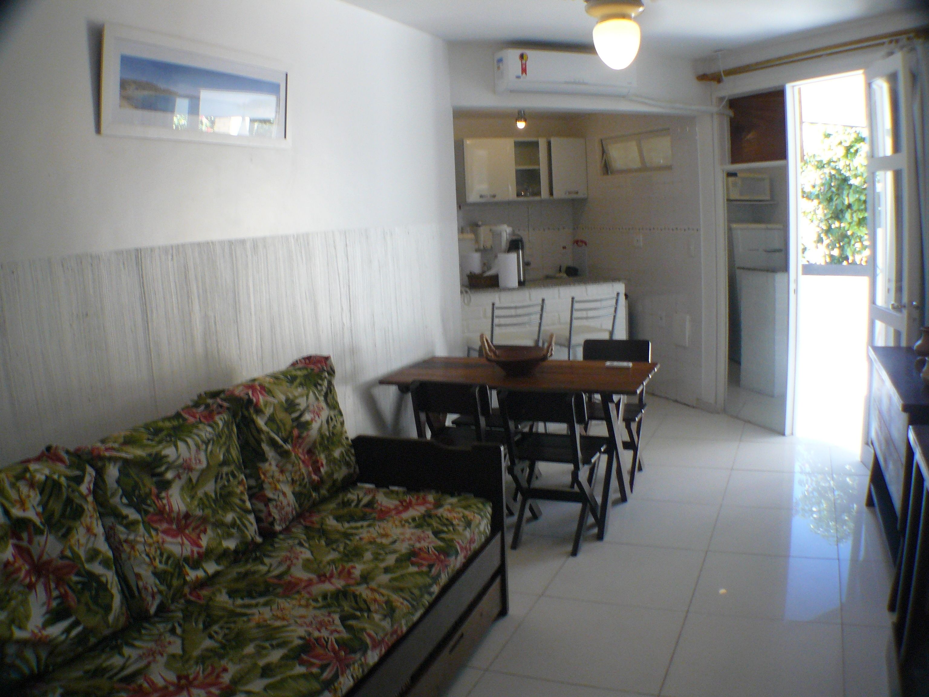 A living room with a floral sofa, a dining table with chairs, and a kitchen area with cabinets and appliances.
