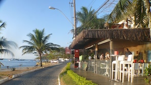 A coastal restaurant with outdoor seating, a thatched roof, and a view of the sea. - BÚZIOS BEACH INTERNACIONAL RESIDENCE SERVICE (Búzios)