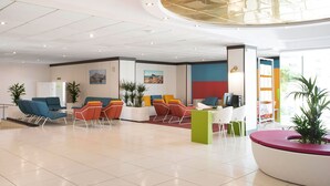 A spacious lobby with modern seating, a central green pillar, and artwork on the walls. - Aparthotel Acuasol (Peniscola)