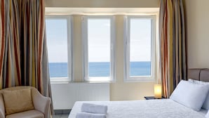 A hotel room with a bed, two windows with curtains, a chair, and a nightstand with a lamp. - Sea Breeze Apartments Chios (Chios)