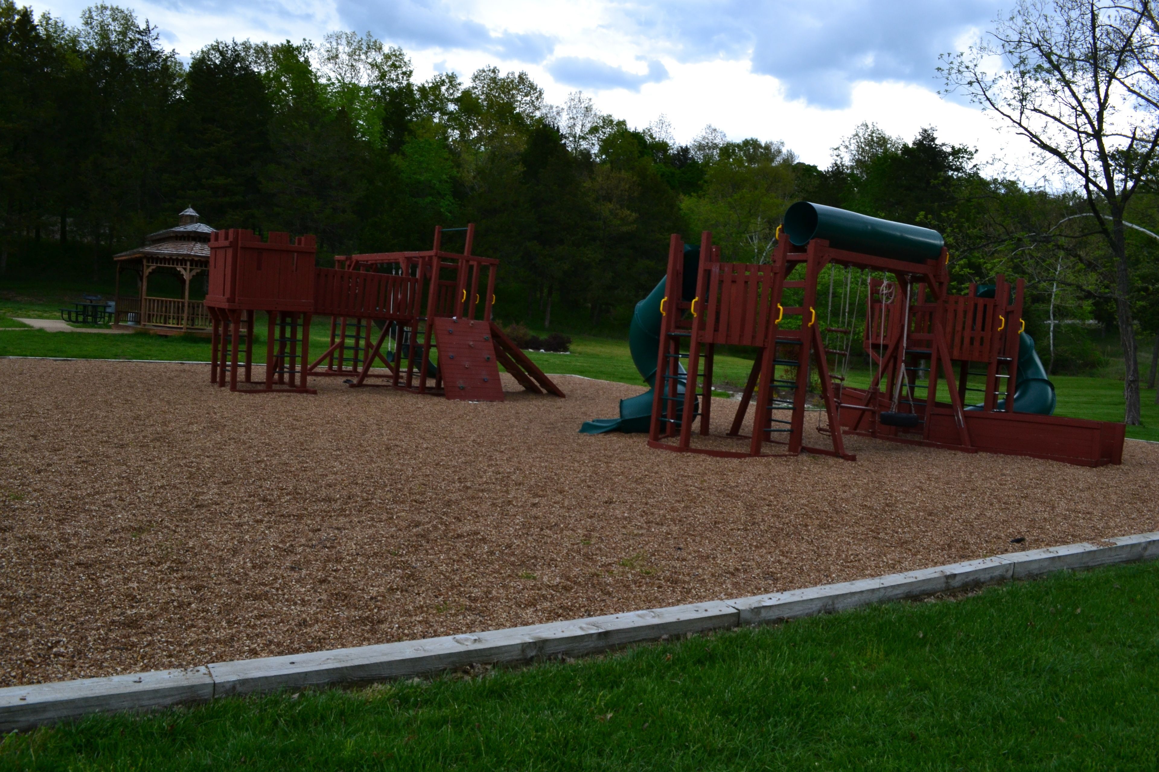 Un parque infantil con estructuras de juego de madera y un tobogán verde.